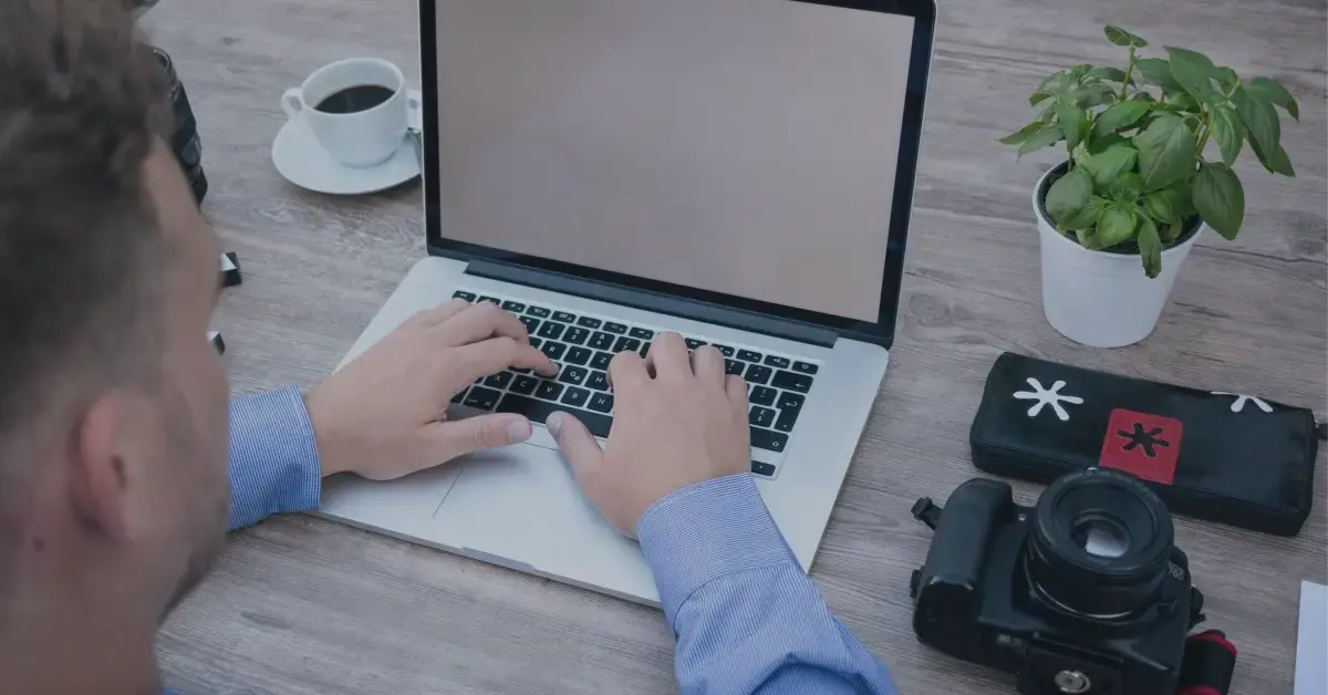 Man working on his laptop next to his camera.