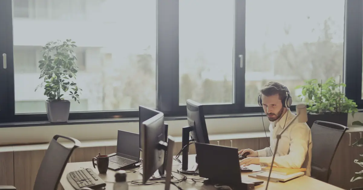 man with headphones working on a computer next to a window