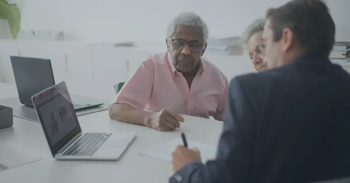 two older people watch a man in a suit write