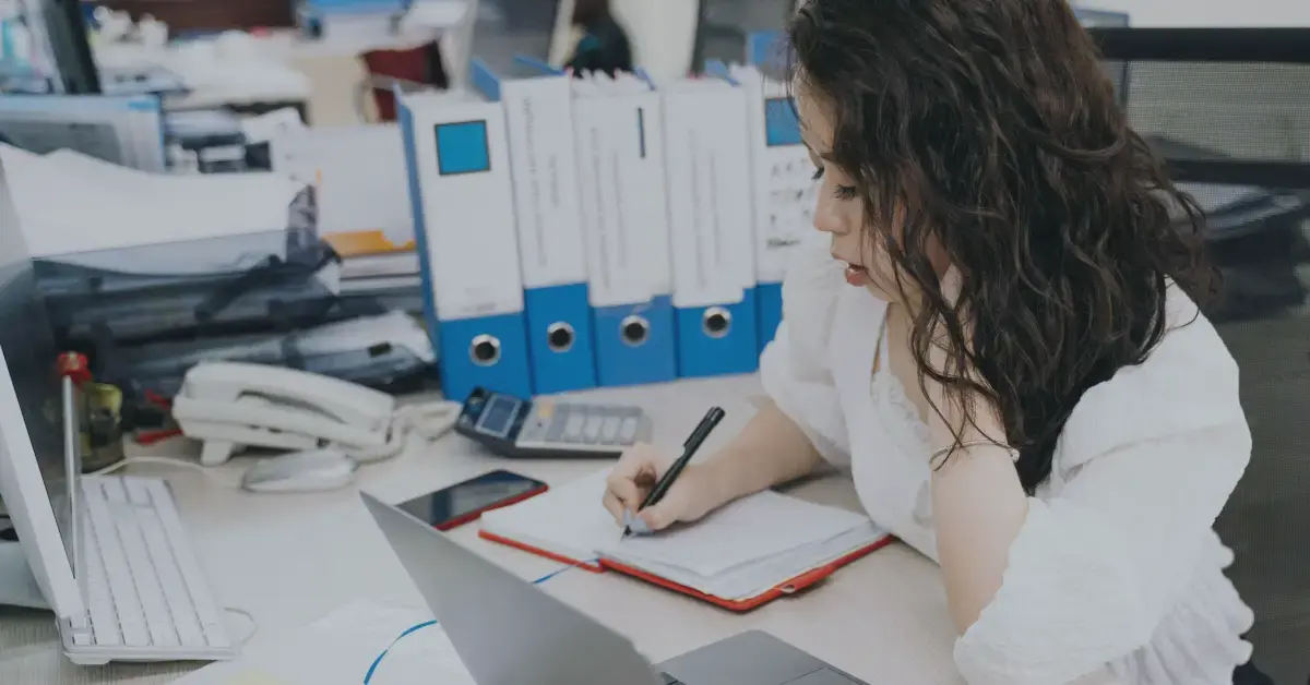 a woman works on a piece of paper with files next to her